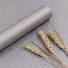 three stalks of wheat next to a rolling pin on a gray surface with silver foil