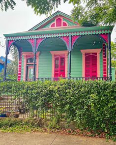 a green and pink house sitting on the side of a road next to a lush green hedge