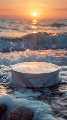 a white object sitting in the middle of some water at sunset or sunrise, with waves crashing around it