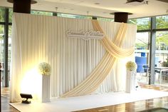 a white stage set up for a wedding ceremony with flowers on the floor and drapes