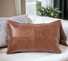 a brown leather pillow sitting on top of a white couch next to a potted plant