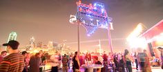 a group of people standing on top of a roof next to a tall neon sign