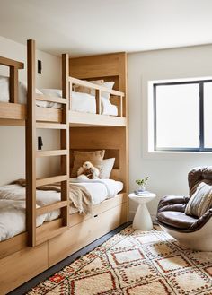 a bedroom with bunk beds and a chair in the corner, next to a window