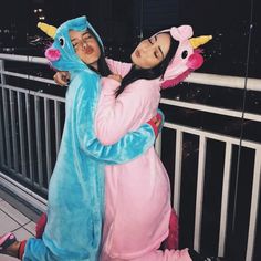 two girls in costumes hugging each other on a balcony overlooking the city at night time