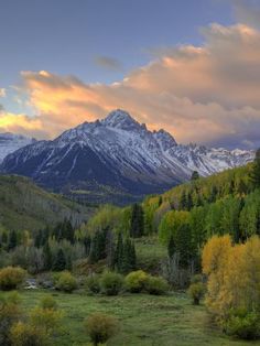 the mountains are covered in snow and trees with yellow leaves on them as the sun sets