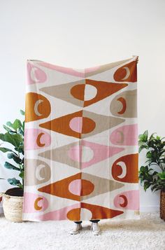 an orange and pink blanket on top of a white rug next to a potted plant