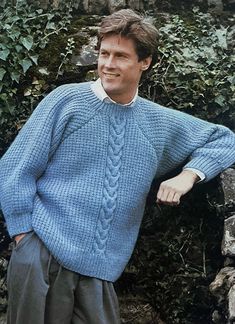 a man standing in front of a stone wall wearing a blue sweater