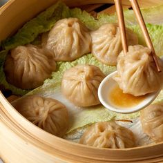 a person holding chopsticks over dumplings in a wooden bowl with lettuce and sauce