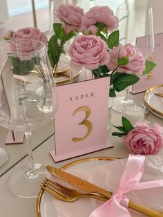 a table set with pink flowers and place cards for the number three, on top of a gold plate