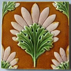 an orange and green tile with white flowers on the bottom, surrounded by smaller leaves