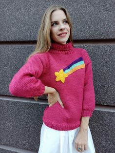 a woman standing next to a wall wearing a pink sweater