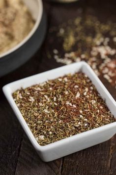 a square white bowl filled with spices on top of a wooden table next to other bowls