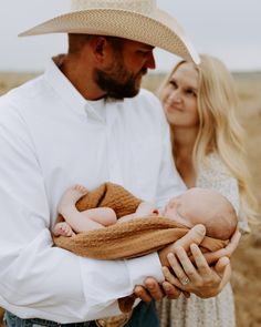 a man holding a baby in his arms while standing next to a woman wearing a cowboy hat