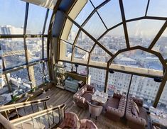 a room with couches, tables and chairs in front of a large window overlooking the city