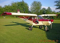 a small red and white plane sitting on top of a lush green field