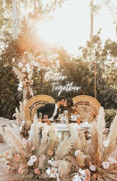 a bride and groom kissing in front of an outdoor table surrounded by pamodia