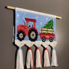 a cross stitch christmas banner with a tractor and tree on the front, hanging from a wooden stick