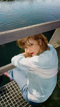 a woman is sitting on the edge of a dock looking at the camera with her hands behind her head