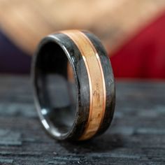 a wooden ring with black and gold inlays sits on top of a table