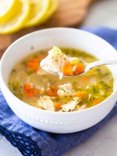 a white bowl filled with chicken soup on top of a blue towel next to sliced lemons