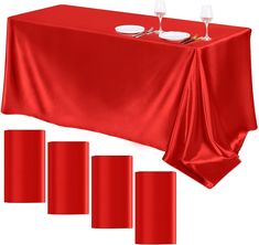 a red table cloth with three place settings and four empty wine glasses on the top