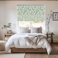 a bed with white sheets and pillows in front of a window covered by green leafy blinds