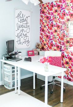 a white desk topped with a laptop computer next to a wall covered in colorful flowers