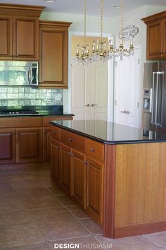 a large kitchen with wooden cabinets and black counter tops, an island in the middle