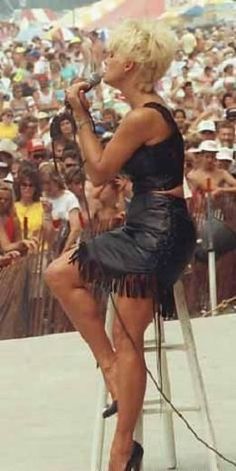 a woman sitting on top of a stool in front of a crowd holding a microphone