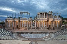 an old roman theatre with columns and seats in the foreground at dusk or dawn