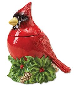 a red bird sitting on top of a planter filled with holly and pine cones