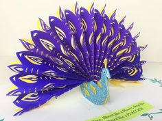 a purple and yellow paper peacock sitting on top of a white table next to a sign