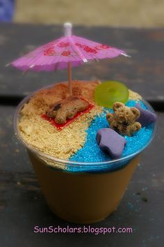 a cup filled with sand and a teddy bear under an umbrella on top of it