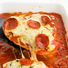 a spatula scooping some pizza sauce out of a casserole dish with pepperoni on top