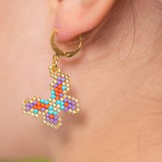 a close up of a person's ear wearing colorful beaded earrings with a cross on it