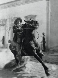 a man riding on the back of a brown horse in front of a white building