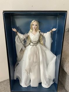 a doll in a blue box with white dress and chains on her arms, holding two hands out