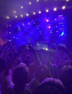 a group of people at a concert with their hands in the air and lights on