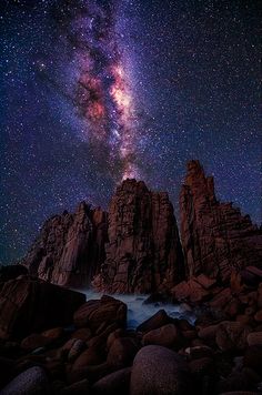 the night sky over some rocks and water