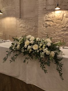 a table with white flowers and greenery is set up in front of a brick wall