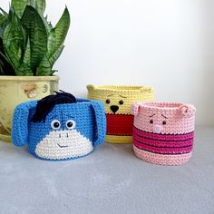 three crocheted pots with faces on them next to a potted plant in the corner