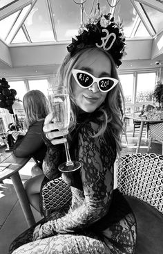 a woman sitting on top of a chair holding a wine glass in her hand and wearing sunglasses