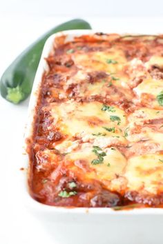 a casserole dish with cheese, sauce and vegetables in it on a white surface