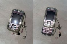 two cell phones with chains attached to them on the ground, one is silver and the other is pink