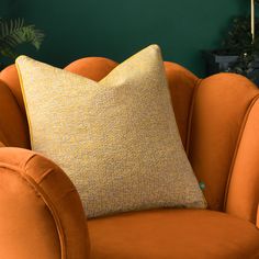 an orange chair with a yellow pillow sitting on it's back in front of a green wall