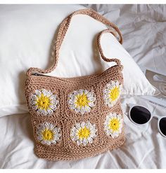 a crocheted purse sitting on top of a bed next to sunglasses