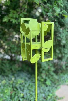 a green sculpture sitting on top of a wooden pole next to a lush green forest