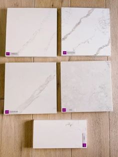 four white marble tiles laid out on a wooden floor with purple and red tags attached to them