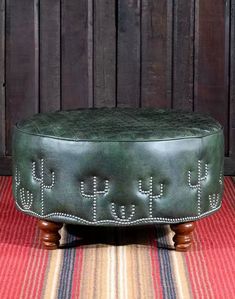 a green leather ottoman sitting on top of a striped rug next to a wooden wall