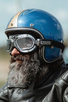 a man with a beard wearing a motorcycle helmet and goggles, looking off to the side